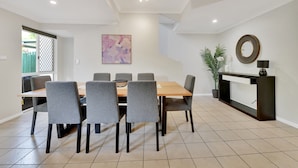 A dining area with a wooden table and grey upholstered chairs, a black console table with a lamp, and a potted plant. - Tranquil 3-Bed Unit with Lush Garden Views (Taringa)