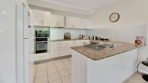 A modern kitchen with white cabinets, a granite countertop, a built-in oven, and a clock on the wall. - Tranquil 3-Bed Unit with Lush Garden Views (Taringa)