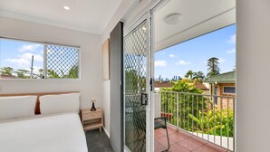 A bedroom with a large bed, a nightstand, a sliding glass door to a balcony, and a view of the city and greenery. - Tranquil 3-Bed Unit with Lush Garden Views (Taringa)