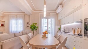 Una cocina moderna con armarios blancos, un comedor con una mesa redonda y sillas, y una sala de estar con un sofá y una planta.