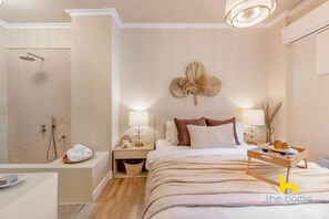 A modern hotel room with a shower, a bedside table with a lamp, a bed with pillows, and a tray with breakfast items. - The Quintessential Getaway with Eclectic Bathroom! (Athina)