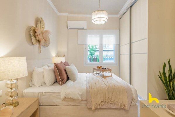 Quarto com cama, mesa de cabeceira, luminária, ar condicionado, janela e uma planta.