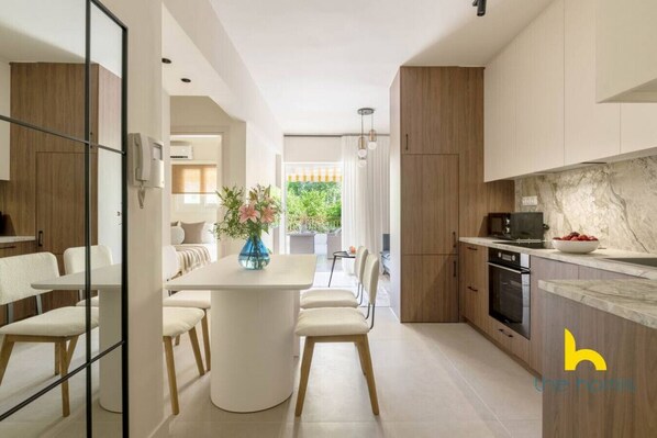 A modern kitchen with a marble countertop, wooden cabinets, and a dining area with a white table and chairs.