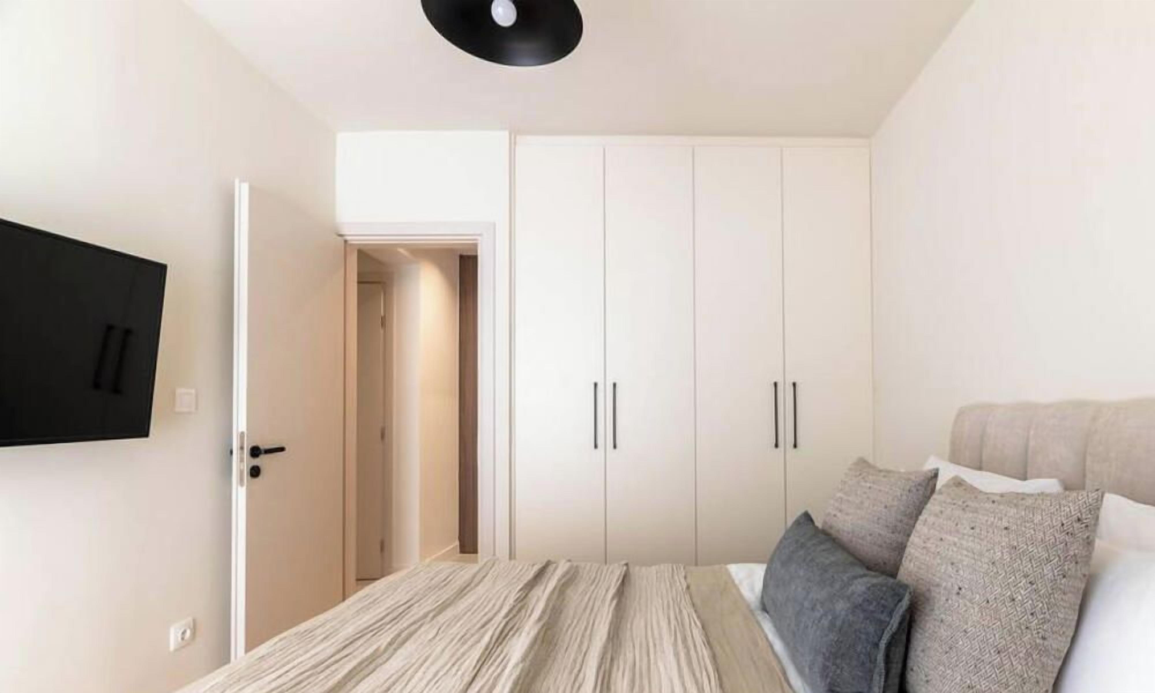 Une chambre à coucher avec un lit, un téléviseur fixé au mur et une armoire.