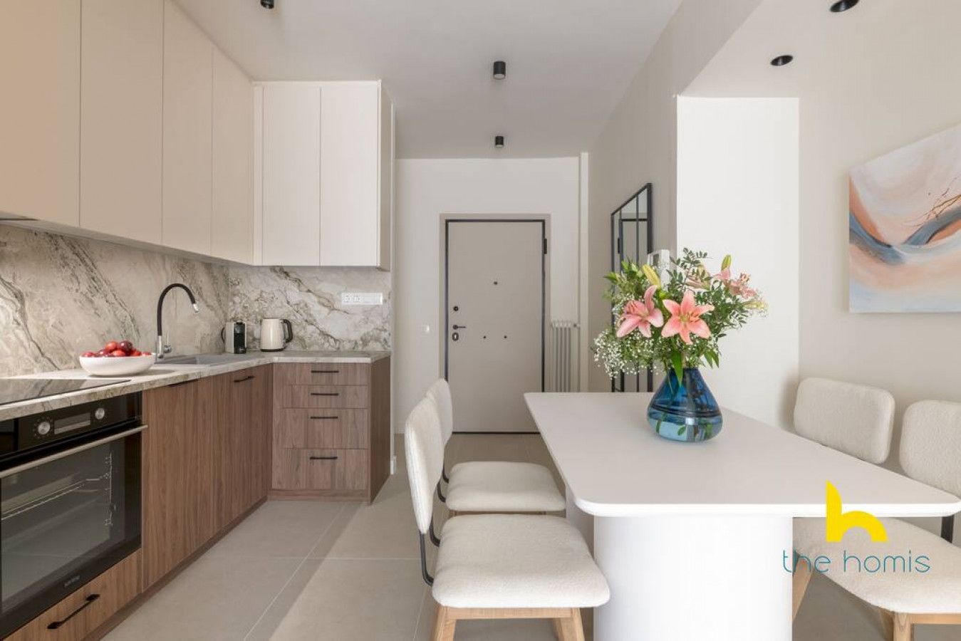 Una cocina moderna con armarios blancos, encimera de mármol y comedor con mesa y sillas blancas.