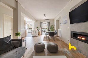 A modern living room with a fireplace, a sofa, ottomans, and a dining area with a table and chairs. - Sunny Athenian Oasis Spacious Family Haven! (Kallithea)