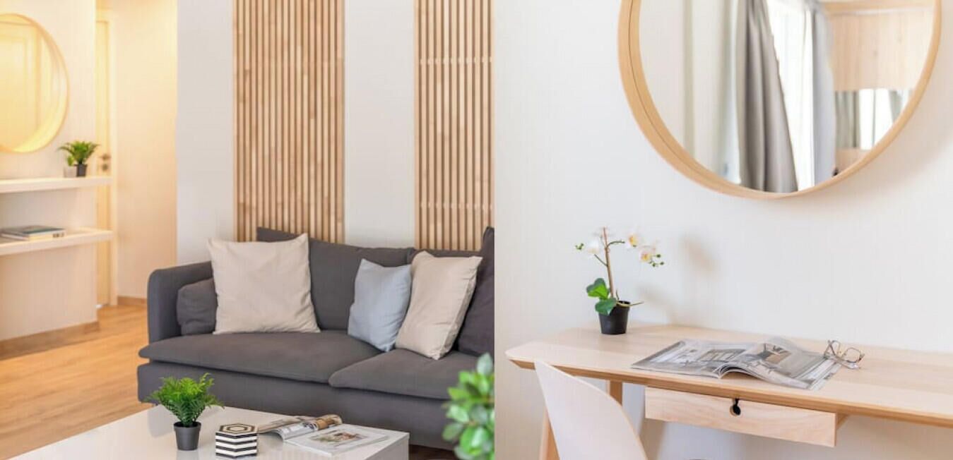 Ein modernes Wohnzimmer mit einem grauen Sofa, einem runden Spiegel, einem kleinen Tisch mit einer Pflanze und einem Bücherregal.