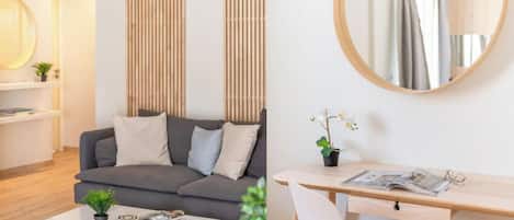 Una sala de estar moderna con un sofá gris, un espejo redondo, una mesita con una planta y una estantería.