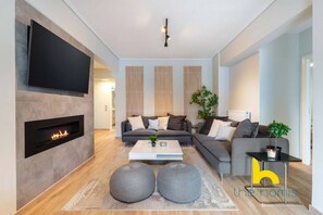 A modern living room with a fireplace, a sofa set, and a television mounted on the wall. - Sunny Athenian Oasis Spacious Family Haven! (Kallithea)