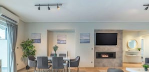 A modern living room with a fireplace, a dining area, and a TV mounted on the wall. - Sunny Athenian Oasis Spacious Family Haven! (Kallithea)