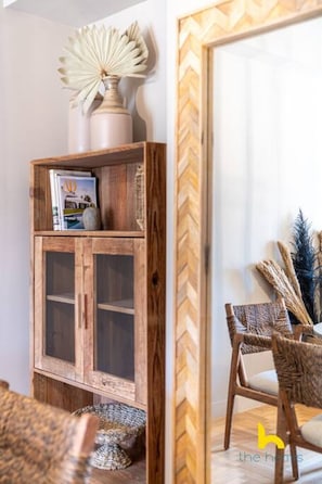 Ein Holzkabinent mit Glastüren, ein gewobener Stuhl und eine dekorative Vase.