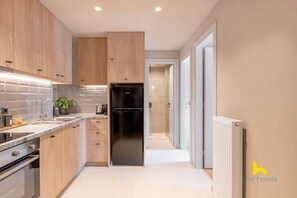 A modern kitchen with wooden cabinets, a black refrigerator, and a white tiled backsplash. - Sun-Kissed Boho Haven with Whirlpool Bliss & Patio (Athina)