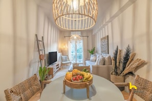 A modern living room with a round table, a television, and a large woven light fixture. - Sun-Kissed Boho Haven with Whirlpool Bliss & Patio (Athina)