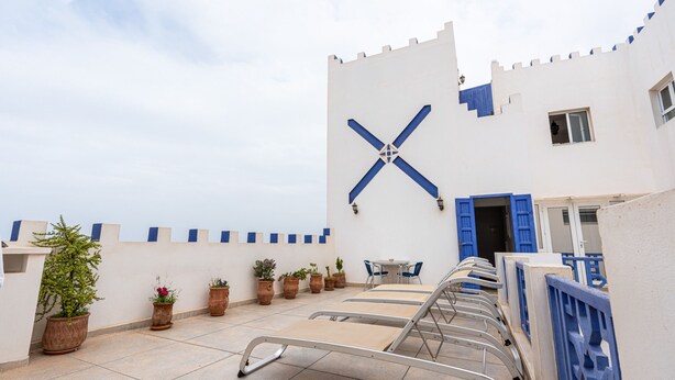 A rooftop terrace with lounge chairs, potted plants, and a castle-like wall design. - Auberge Azul ifni (Sidi Ifni)