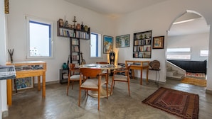 A spacious living area with a dining table, chairs, bookshelves, and artwork. - Auberge Azul ifni (Sidi Ifni)