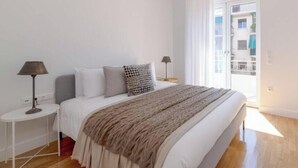 Un dormitorio moderno con una cama grande, dos mesitas de noche, una lámpara colgante y vistas al balcón exterior.