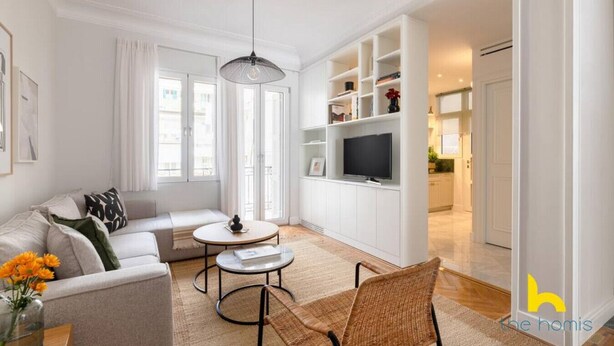 Una sala de estar moderna con un sofá, dos sillones, una mesita de centro y un televisor sobre un mueble blanco.