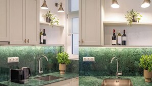 Una cocina moderna con encimera de mármol verde, un lavamanos integrado, una cafetera y botellas de vino en los estantes.