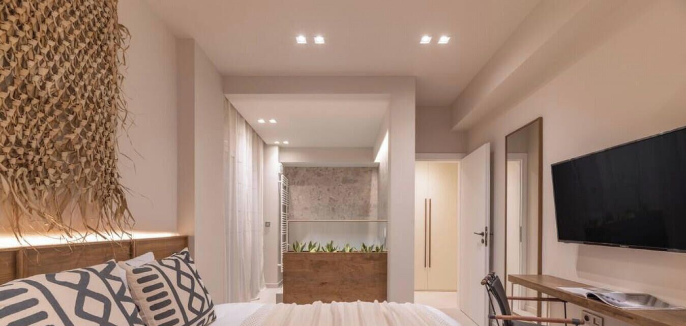 A modern hotel room with a bed, a TV, a shower area, and a wooden side table.