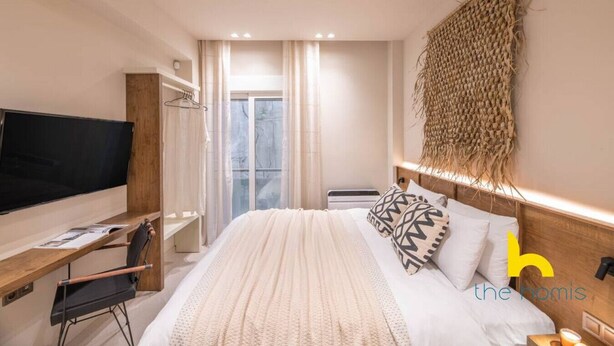 A modern bedroom with a large bed, a TV, a desk, and a window with curtains. - Charming Boho Haven Luxurious Escape in Thisseio! (Athina)