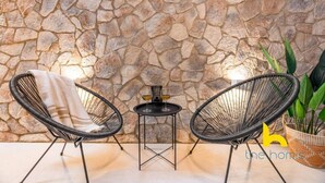 A stone wall, two wicker chairs, a small table with a lamp, and a potted plant. - Charming Boho Haven Luxurious Escape in Thisseio! (Athina)