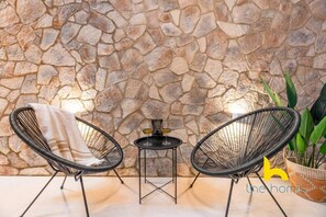 A stone wall, two wicker chairs, a small table with a lamp, and a potted plant. - Charming Boho Haven Luxurious Escape in Thisseio! (Athina)