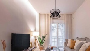A modern living room with a flat-screen TV, a coffee table, a sofa, and a potted plant. - Charming Boho Haven Luxurious Escape in Thisseio! (Athina)