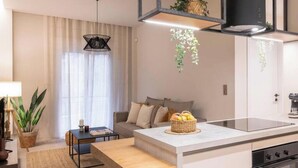 A modern kitchen with a central island, a dining area with a sofa and table, and a hanging plant. - Charming Boho Haven Luxurious Escape in Thisseio! (Athina)