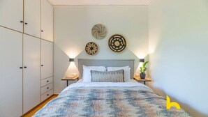 A bedroom with a bed, bedside tables, a wardrobe, and decorative wall art. - Riviera Haven - Serene Sunny Retreat Near Seaside! (Vouliagmeni)
