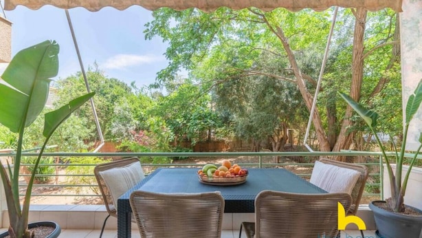 An outdoor patio with a table and chairs, surrounded by potted plants and trees. - Riviera Haven - Serene Sunny Retreat Near Seaside! (Vouliagmeni)