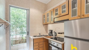 A modern kitchen with wooden cabinets, a stainless steel refrigerator, and a window providing a view of greenery. - Riviera Haven - Serene Sunny Retreat Near Seaside! (Vouliagmeni)