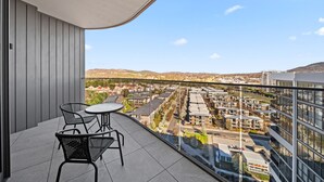 Een balkon met een tafel en stoelen, met uitzicht op een woongebied met gebouwen en heuvels in de verte.
