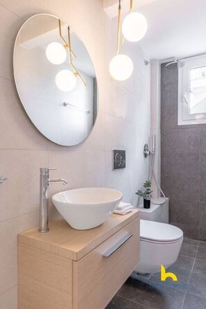A modern bathroom with a round mirror, a vessel sink, a toilet, and a shower area. - Spacious 3BR Retreat w/ 2 Baths + Fast Wi-Fi (Vironas)