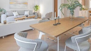Uma sala de estar moderna com uma grande mesa de jantar de madeira, cadeiras xadrez, um sofá e uma mesa de centro.