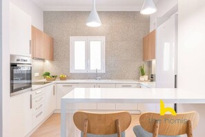 Moderni keittiö, jossa on valkoiset kaapit, keskellä oleva keittiösaareke ja riippuvalaisimet.