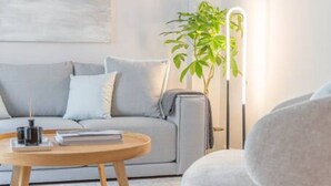 Uma sala de estar moderna com um sofá cinza, uma mesa de centro redonda de madeira, uma poltrona cinza e um abajur alto.