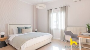 Quarto moderno com cama, mesas de cabeceira, escrivaninha, cadeira, janela com cortinas e ar condicionado.