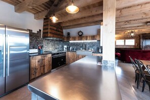 A modern kitchen with a large island, stainless steel appliances, and a rustic wooden ceiling.