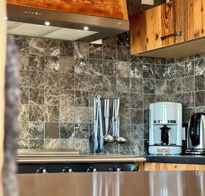 A kitchen with a marble backsplash, stainless steel appliances, and wooden cabinets. - Chalet Les Papis ⭐ Heated Pool • Sauna • Lake View • Gérardmer (Gérardmer)
