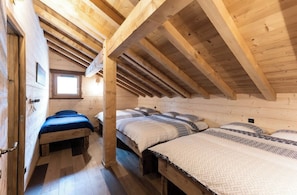 A wooden cabin with a sloped ceiling, multiple beds, and a window.