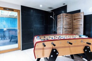 Una habitación moderna con mesa de futbolín, zona de ducha y puerta corredera de vidrio que da a un espacio exterior.