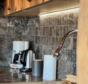 A kitchen with a stainless steel coffee maker, a kettle, a paper towel holder, and a wooden cabinet. - Chalet Les Papis ⭐ Heated Pool • Sauna • Lake View • Gérardmer (Gérardmer)