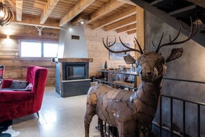 Un interior rústico con techo de madera, chimenea, una silla roja y una escultura de ciervo.