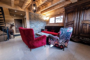 A wooden interior with a red sofa, patterned armchair, and a stone wall.