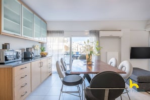 A modern kitchen with a dining area, including a table with chairs, a coffee machine, and a TV mounted on the wall. - 3-Storey Family Home, City View & Private Parking! (Athina)