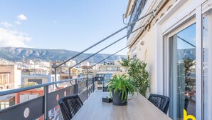 A balcony with a wooden table and chairs, a potted plant, and a view of the city and mountains. - 3-Storey Family Home, City View & Private Parking! (Athina)