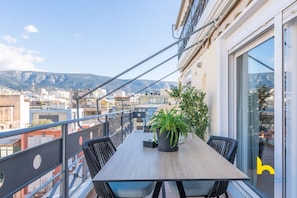 A balcony with a wooden table and chairs, a potted plant, and a view of the city and mountains. - 3-Storey Family Home, City View & Private Parking! (Athina)