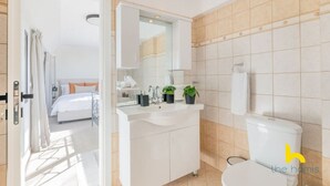 A modern bathroom with a white sink, mirror, and toilet. There is a bed visible through an open door in the adjacent room. - 3-Storey Family Home, City View & Private Parking! (Athina)