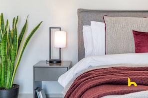 A neatly arranged bedroom with a bed, bedside table, lamp, and a potted plant. - 3-Storey Family Home, City View & Private Parking! (Athina)