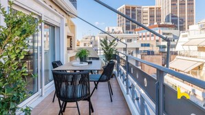 A balcony with a table and chairs, overlooking a cityscape with modern buildings. - 3-Storey Family Home, City View & Private Parking! (Athina)
